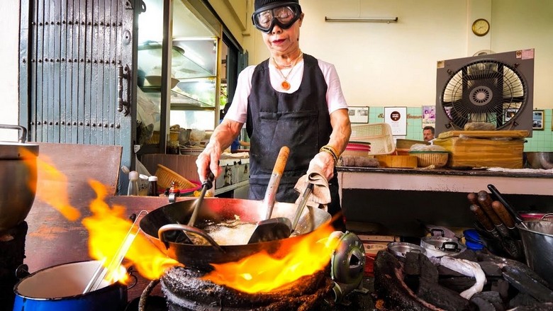 Góc bếp mở của quán tom yum vỉa hè Bangkok, đầu bếp đang múc canh vào tô sứ trắng