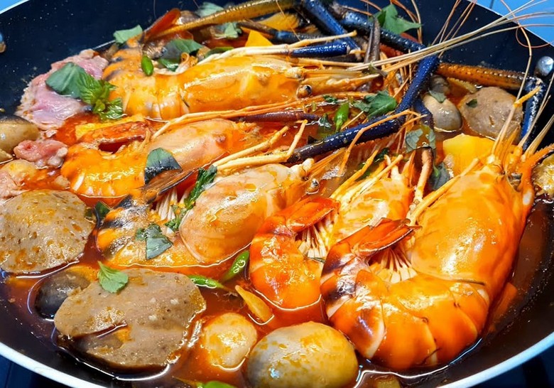 Nồi lẩu Tom Yum đỏ cam đang sôi trên bếp, có tôm và nấm